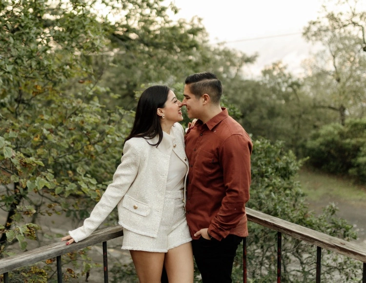 Pareja sonriendo con ternura mientras se miran frente a un paisaje natural, reflejando amor y conexión.