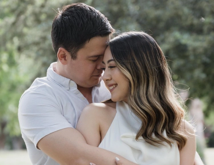 Pareja abrazada en un parque, compartiendo una sonrisa íntima antes del gran día.
